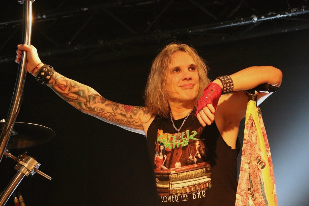 Rockmusiker auf Bühne mit Mikrofon und Tattoos.